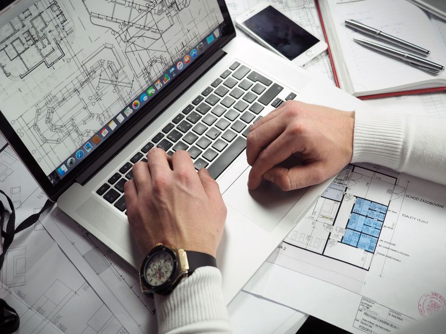 A clean, modern architect's desk with rolled blueprints, a hard hat, and an open laptop, representing the intersection of traditional planning and modern technology.