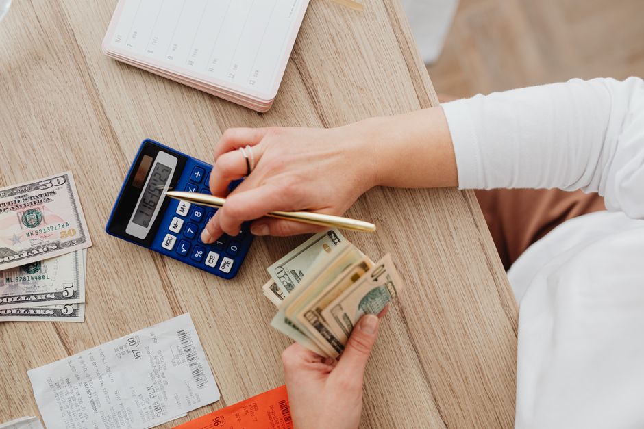 Person sits at a modern wooden table with a calculator and documents, carefully reviewing the finances for selling their h...