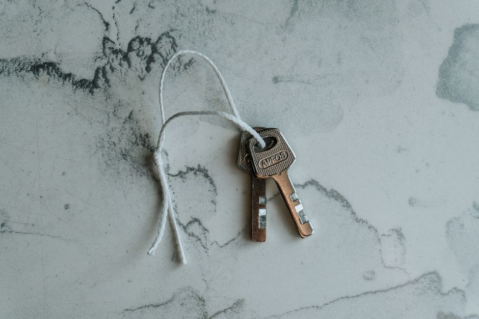 A set of modern house keys rests on a clean surface next to a small, neat stack of coins, symbolizing the concept of real estate commissions and savings.